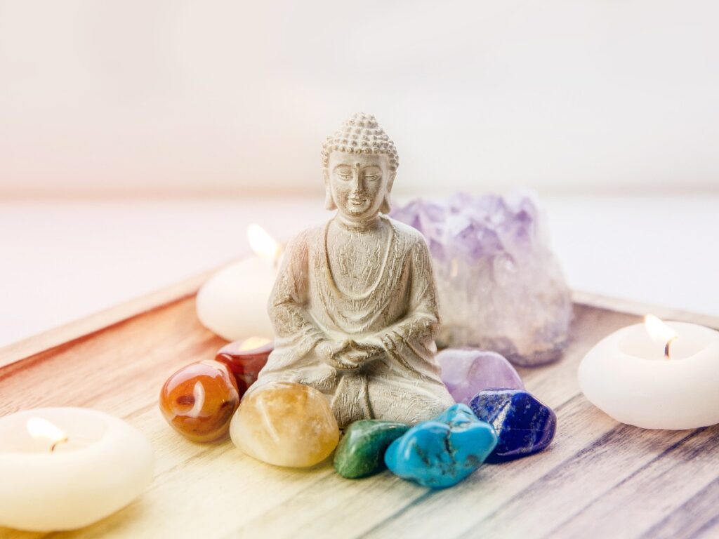 All seven chakra colors crystals stones around sitting buddha figurine on natural wooden tray balance and calm energy flow in home concept jpg